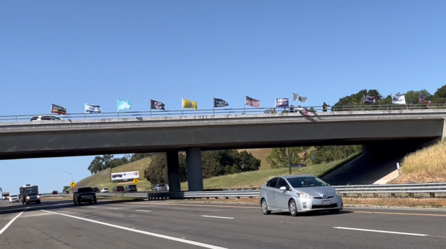 An image of protestors waving 13 flags on the Templeton Bridge in Templeton, CA