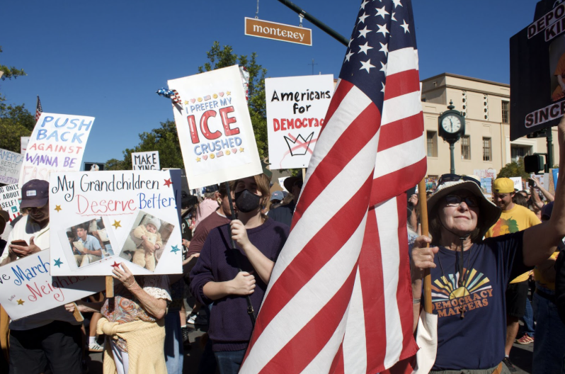 Protesters gather waving flags and signs on the corner of Monterey Street and Los Osos Street in downtown San Luis Obispo for the nationwide “No Kings” protest on Oct. 18.
