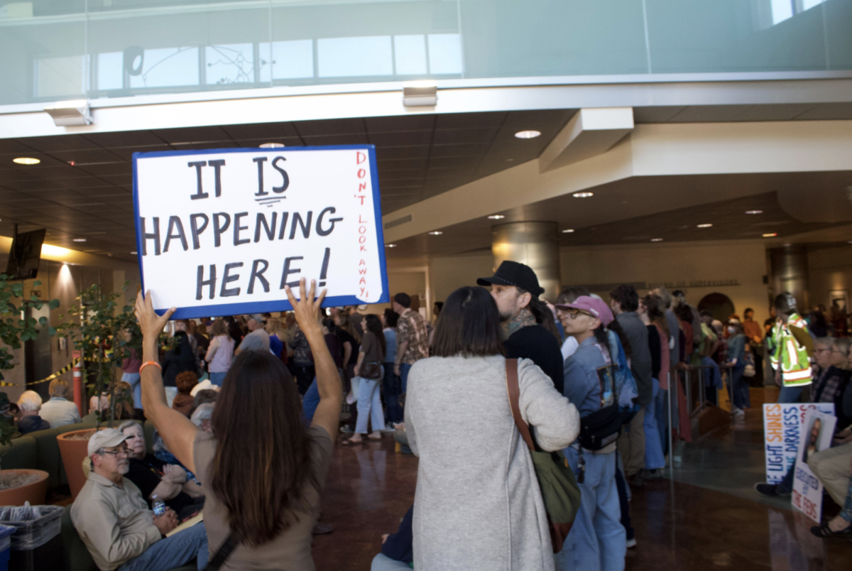 A protester walks through the lobby full of community members waiting for public comment during the TRUTH forum on Jan. 27, 2026, holding a sign with photos of ICE agents recently spotted in SLO County with the message: “It is happening here!"
