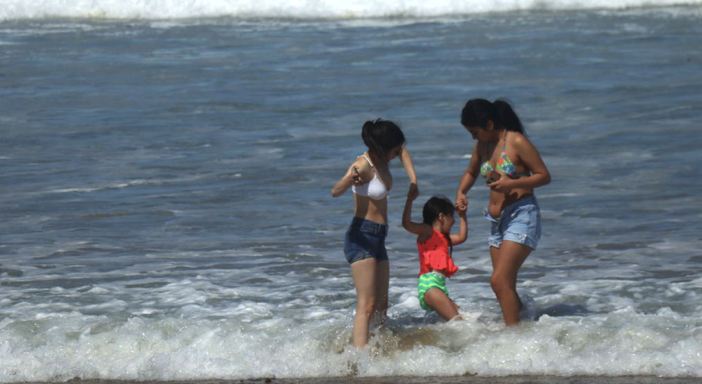 Young girls playing together at Del Monte Beach in Monterey during summer 2025. The older girls are helping the little one over the waves.
