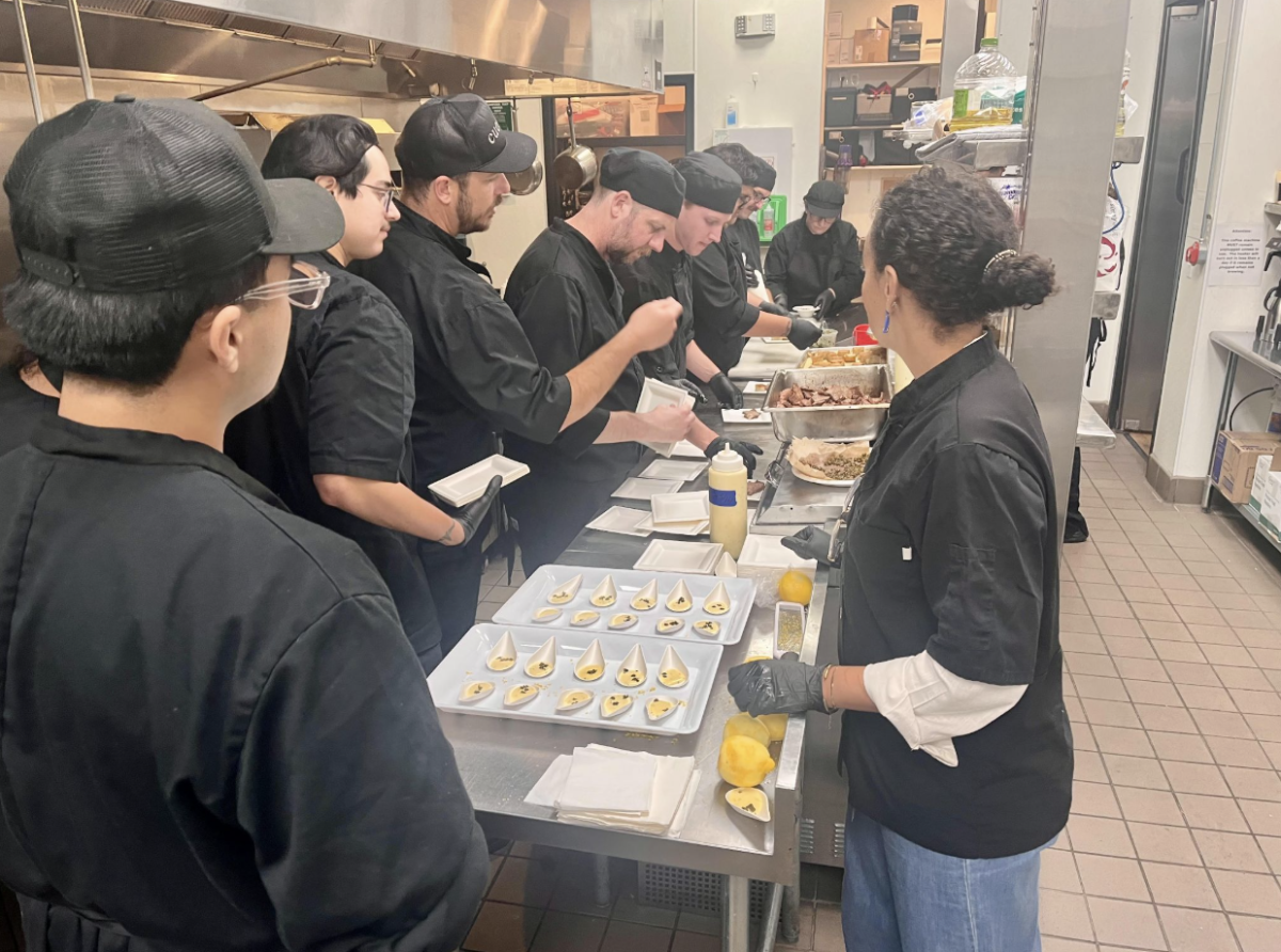Chef Graham Yates (instructor for the CUL 220 class featured in the photo) and Chef Zoe Elliott assist students as they prepare food for their Jazz Night final project in downtown SLO. Image courtesy of Cuesta Culinary